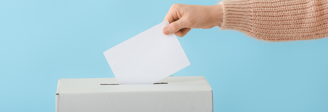 Eine Person wirft ein Couvert in eine Wahlurne